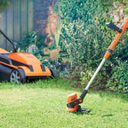 Orange lawn mower and trimmer on a grassy lawn with garden background
