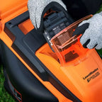 Orange and black lawn mower with a battery being inserted, on grass.