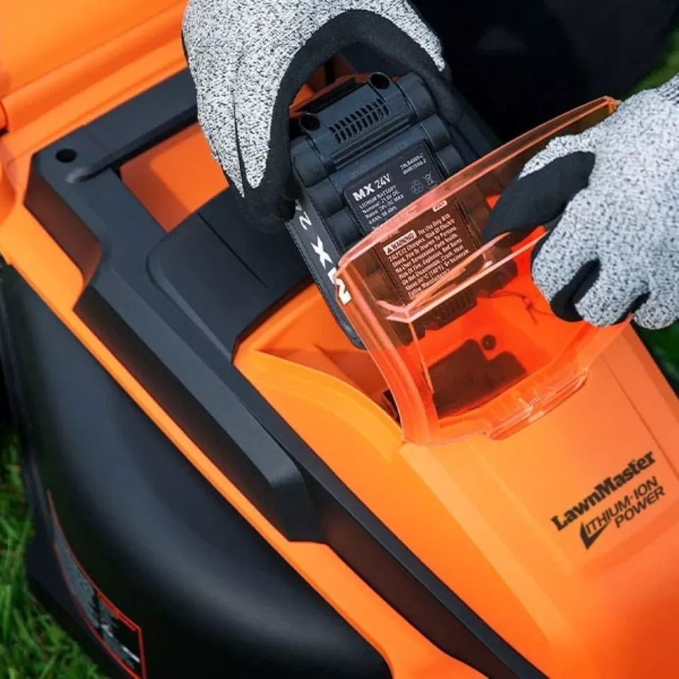 Orange and black lawn mower with a battery being inserted, on grass.