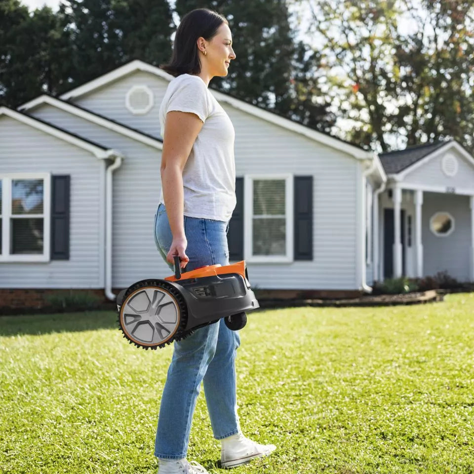 Woman carrying a lawn mower on a grassy lawn with a house in the background