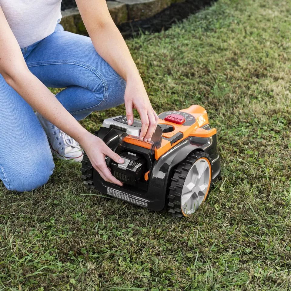 Person adjusting a robotic lawn mower on grass