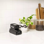 Black MX tool on a kitchen counter with a plant and jars in the background