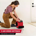 Person using a red air mover with text about air speed settings on a white floor.