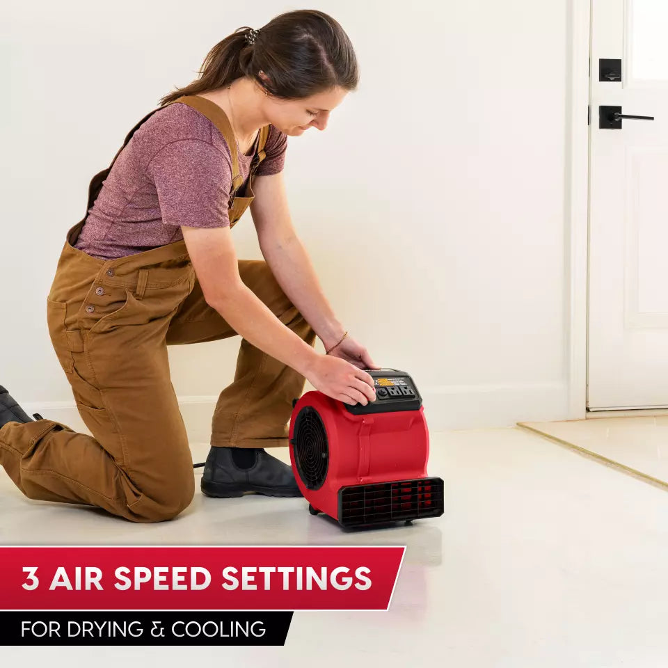 Person using a red air mover with text about air speed settings on a white floor.