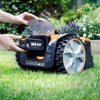 Robotic lawn mower on grass with a person's hand holding its cover