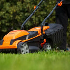 Orange and black lawn mower being used on a grassy area with a blurred background