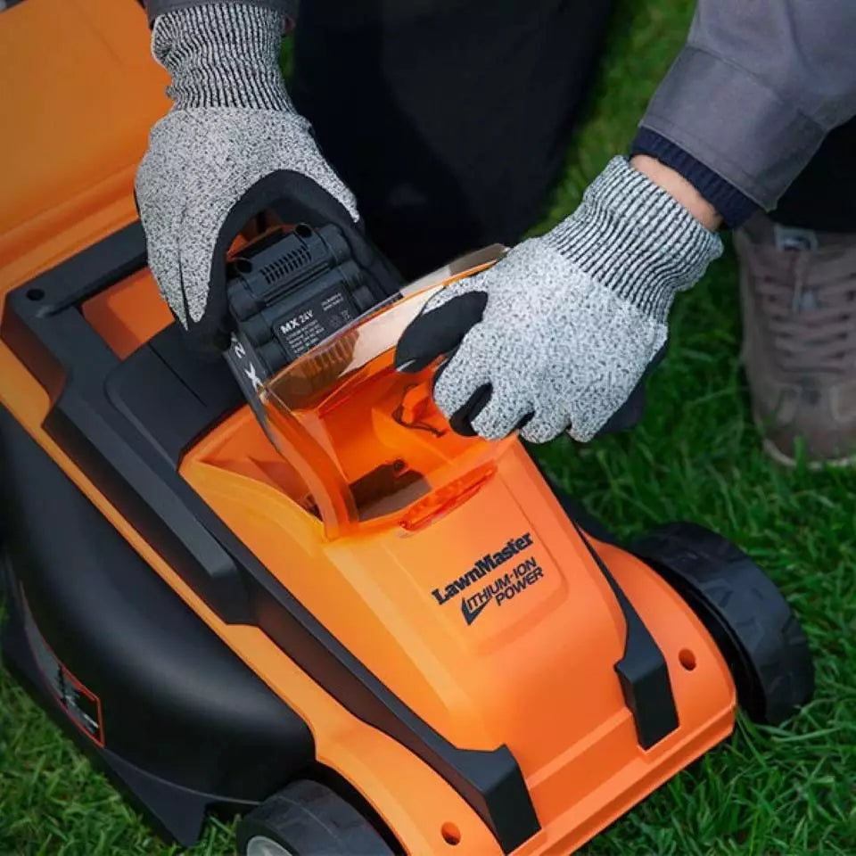 Person wearing gloves attaching a battery to an orange and black lawn mower on grass.