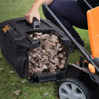 Person using a leaf blower to collect leaves in a black container on a grassy area.
