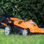 Orange and black lawn mower on grass with blurred greenery in the background