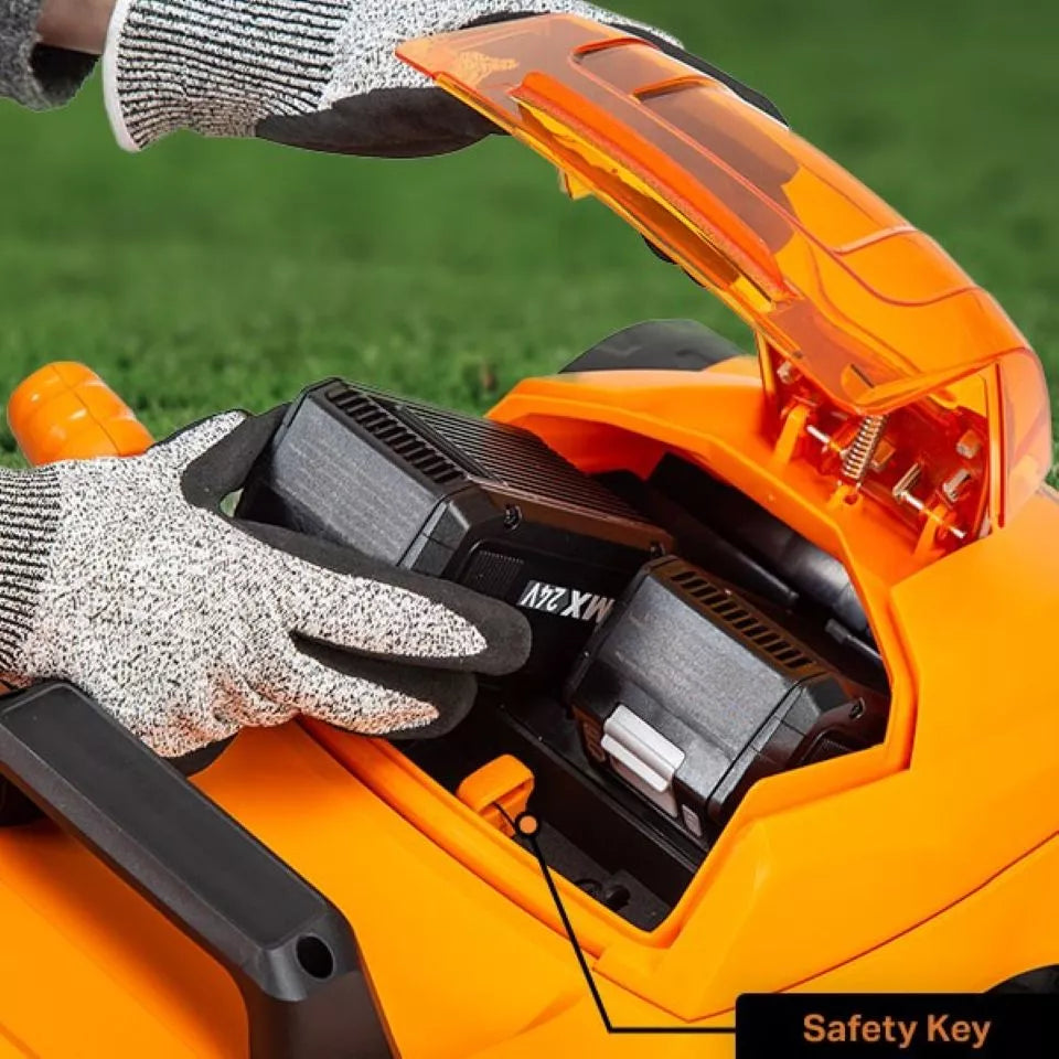 Orange power tool with a safety key feature, held by gloved hands against a grassy background.