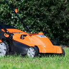 Orange and black lawn mower on grass with a blurred green bush in the background