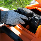Person wearing a gray glove inserting a battery into an orange and black power tool with grass in the background.