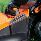 Person adjusting settings on an orange and black lawn mower with a close-up of the control panel.
