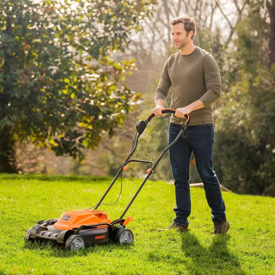 Man using a lawn mower on a grassy area with trees in the background