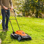 Person using a lawn mower on a grassy area with trees in the background