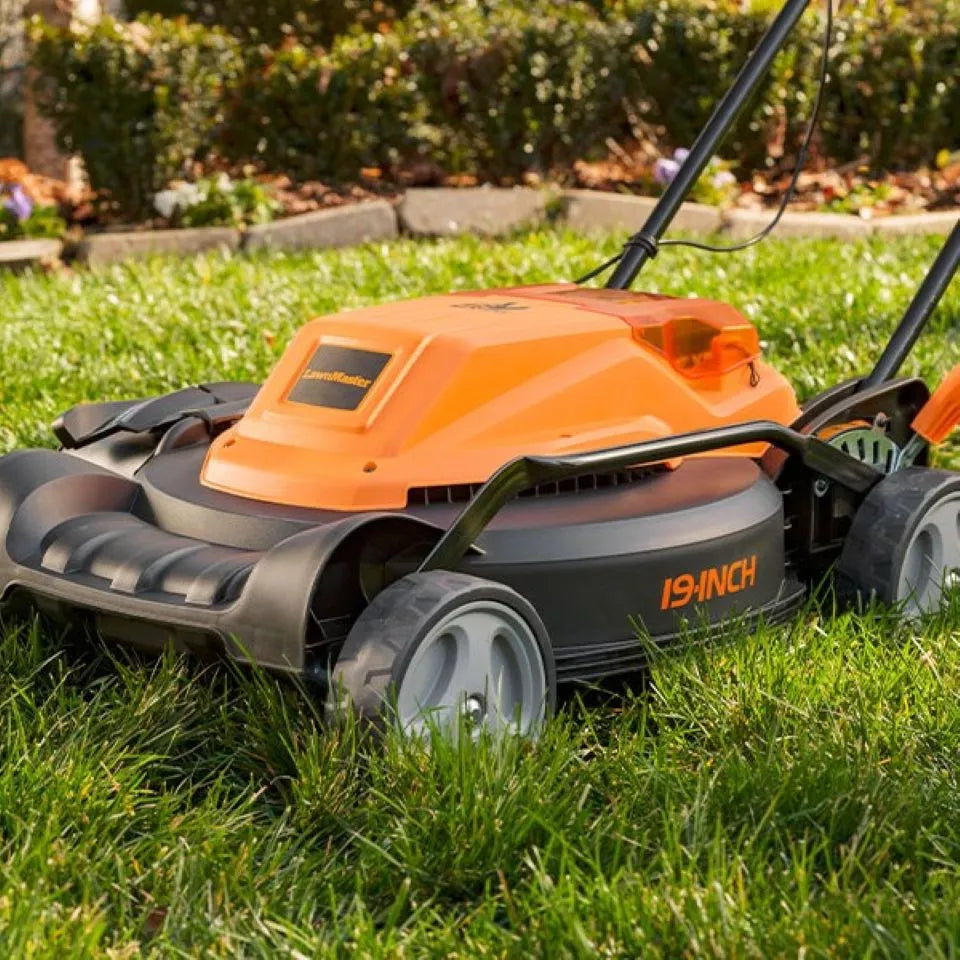 Orange and black lawn mower on a grassy area with bushes in the background