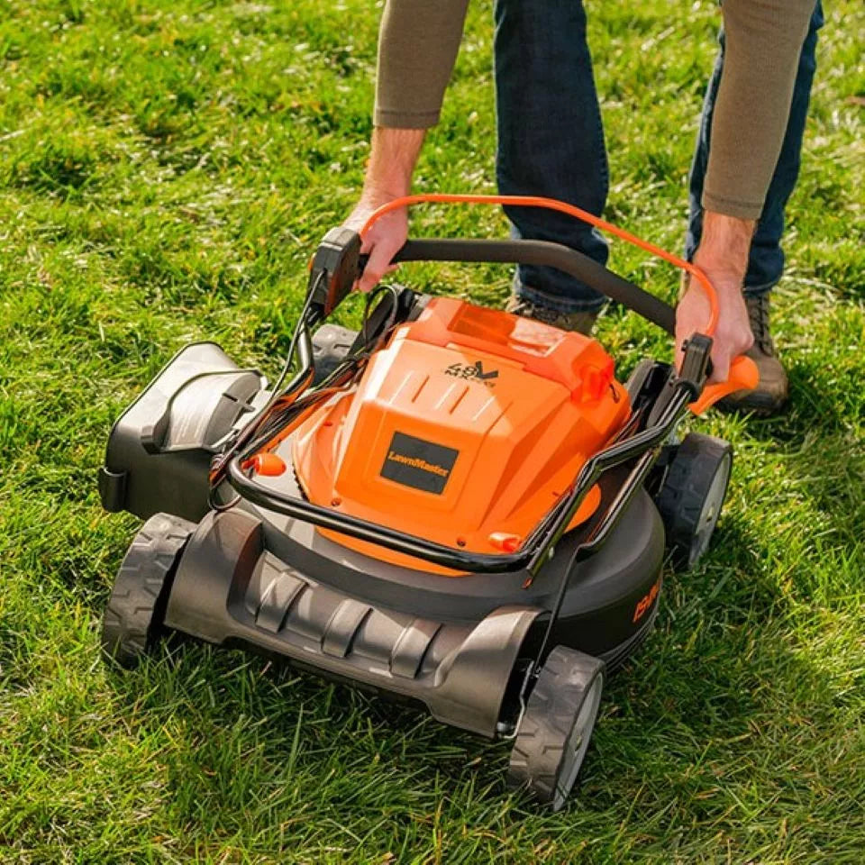 Person using an orange and black lawn mower on grass