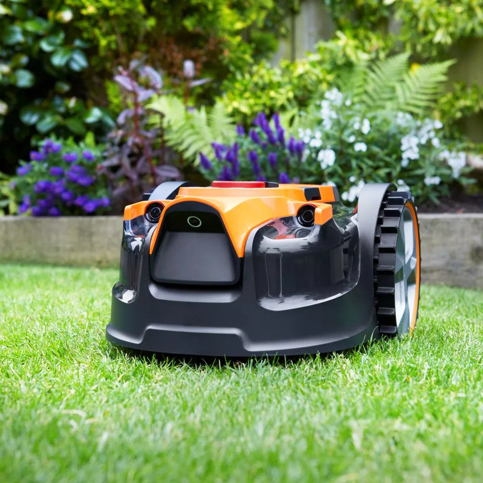 Robotic lawn mower on a grassy lawn with flowers in the background