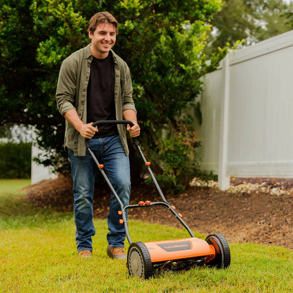 Man mowing grass with a push lawn mower in a garden setting