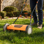 Person using a LawnMaster lawn mower on a grassy area with a garden in the background.
