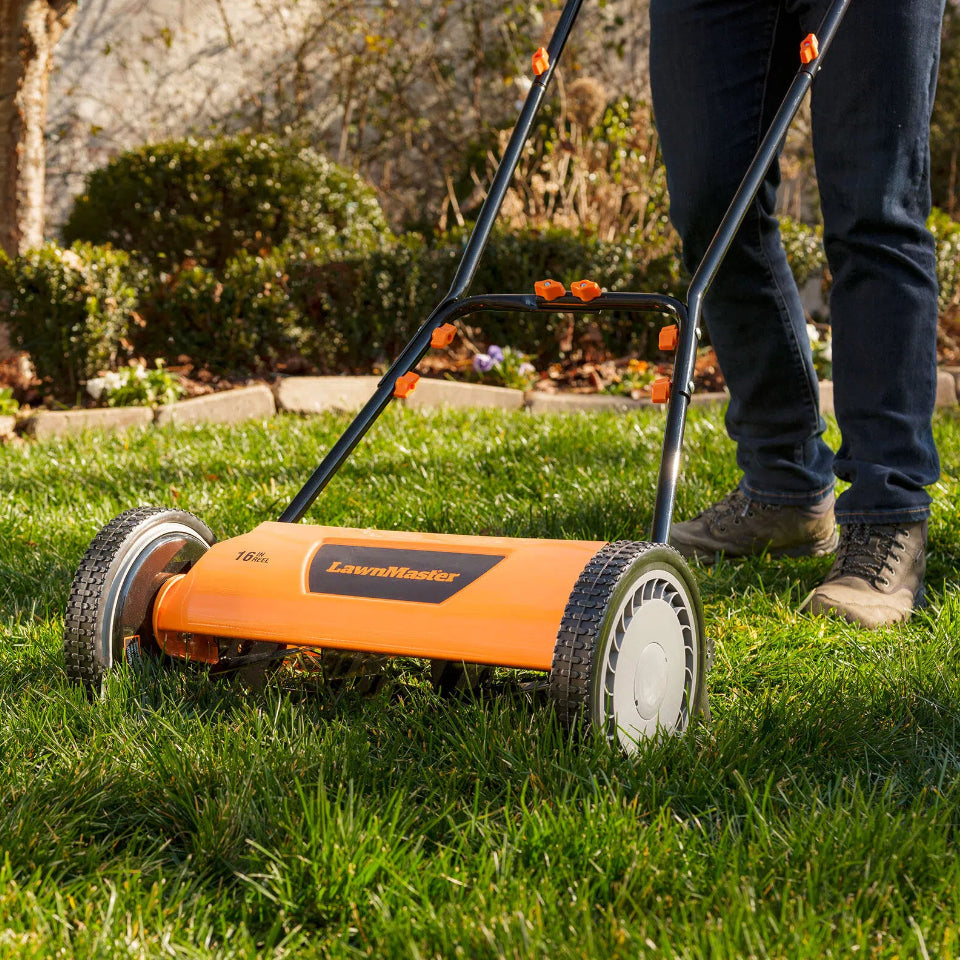 Person using a LawnMaster lawn mower on a grassy area with a garden in the background.