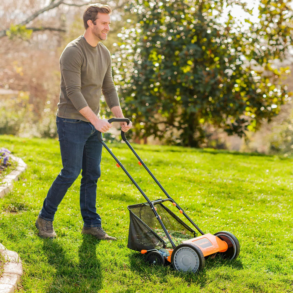 Man mowing a lawn with a push mower in a garden setting