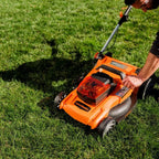 Person using an orange and black lawn mower on a grassy area