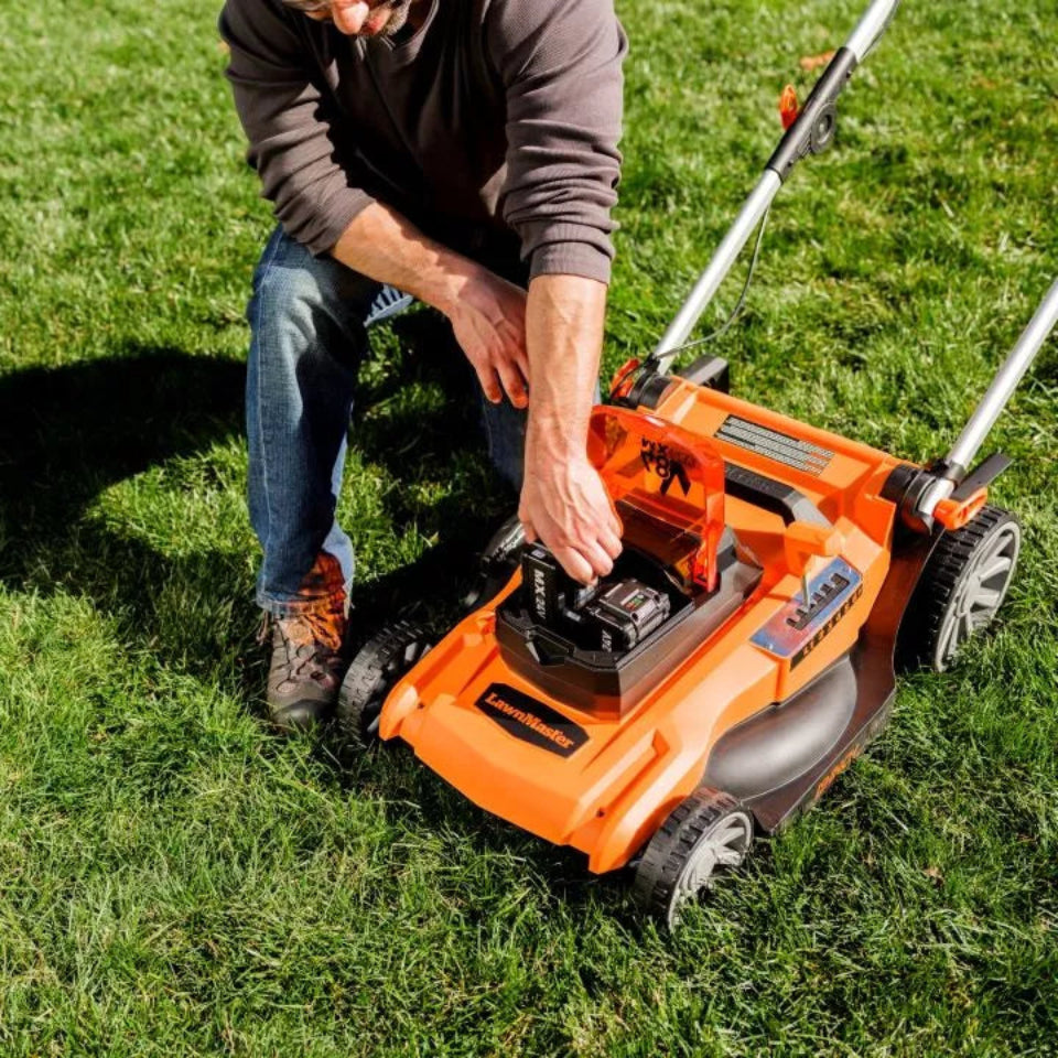 Person adjusting an orange lawn mower on a grassy area