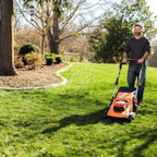 Man using a lawn mower on a green lawn with trees and a house in the background