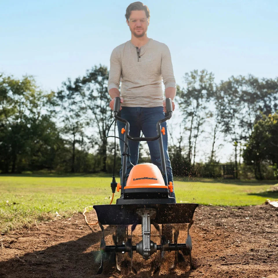Man operating a tiller in a garden with trees in the background