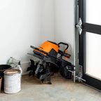 Black and orange snow blower against a white wall with a door open