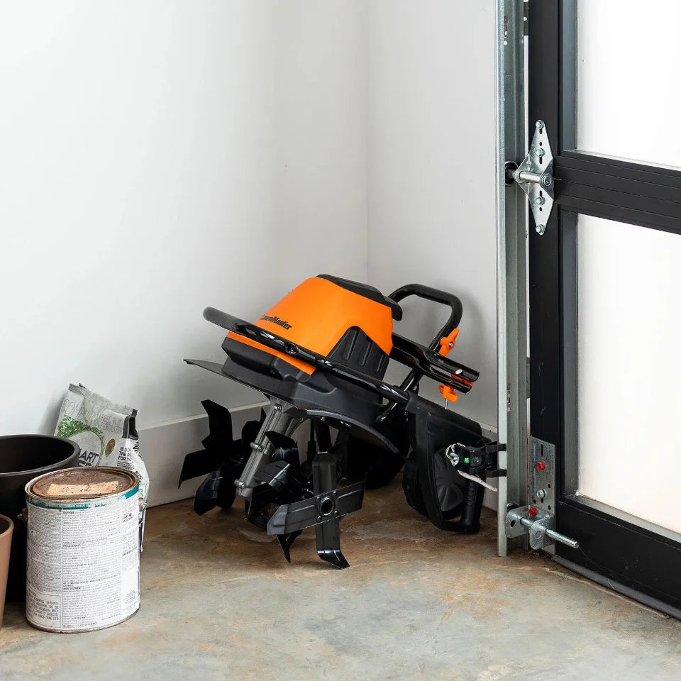 Black and orange snow blower against a white wall with a door open