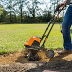 Person using a tiller on a garden bed with trees in the background
