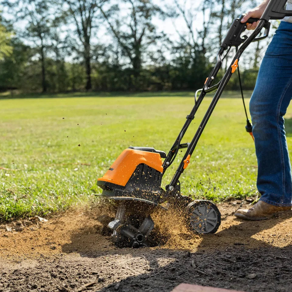 Person using a tiller on a garden bed with trees in the background