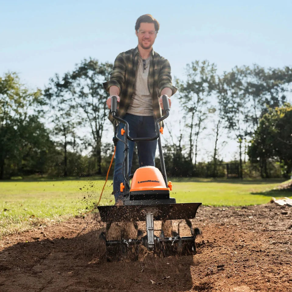 Person using a tiller in a garden with trees in the background