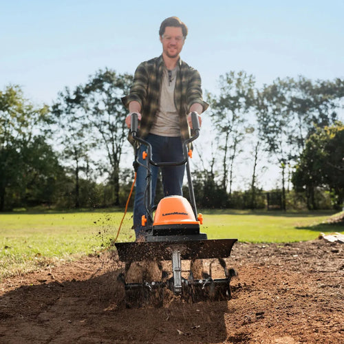 Person using a tiller in a garden with trees in the background