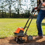 Person using a tiller on a grassy area with trees in the background