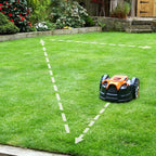 Robotic lawn mower on a green lawn with garden in the background