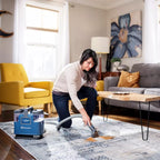 Woman cleaning a rug with a blue vacuum cleaner in a living room.