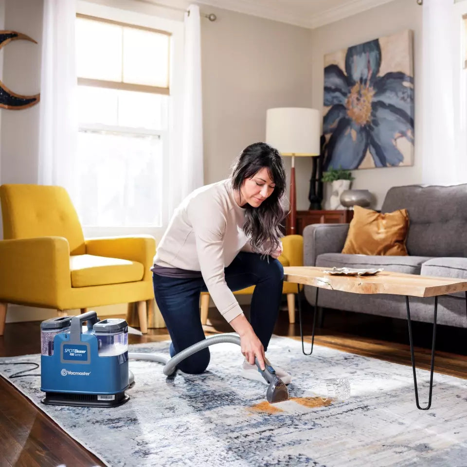 Woman cleaning a rug with a blue vacuum cleaner in a living room.