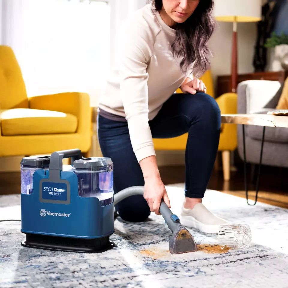Person using a Vacmaster SpotCleaner to clean a rug in a living room.