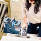 Person using a Vacmaster Spot Cleaner on a rug with a blue cleaning machine in the foreground.