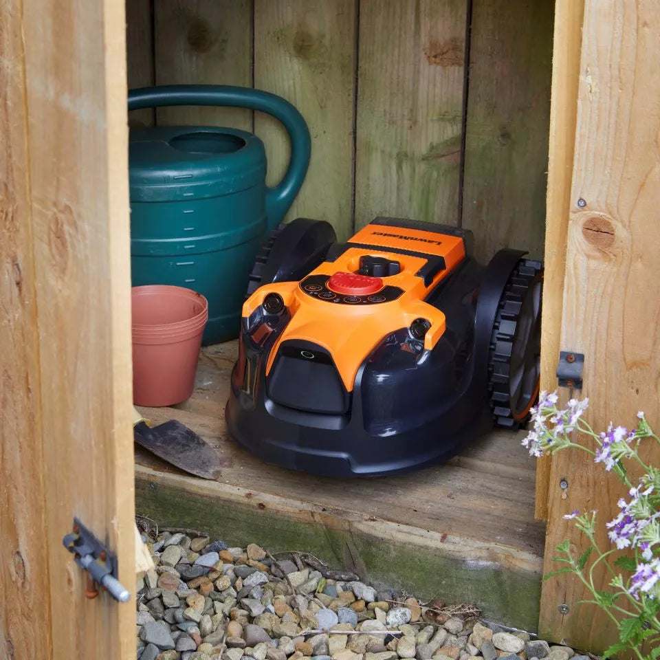 Robotic lawn mower inside a wooden shed with gardening tools and plants.