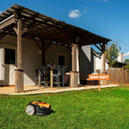 Robotic lawn mower on grass in front of a house with a covered patio