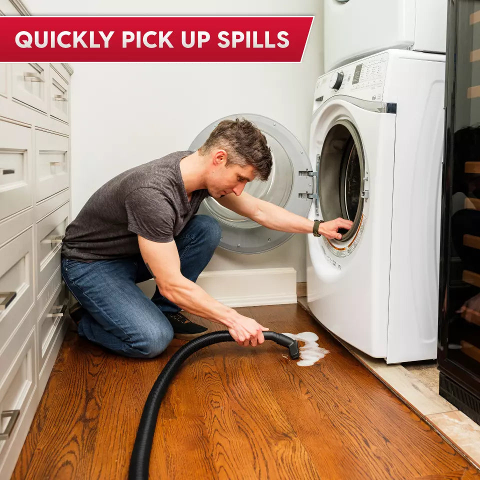 Person cleaning a wooden floor with a vacuum cleaner in front of a washing machine.