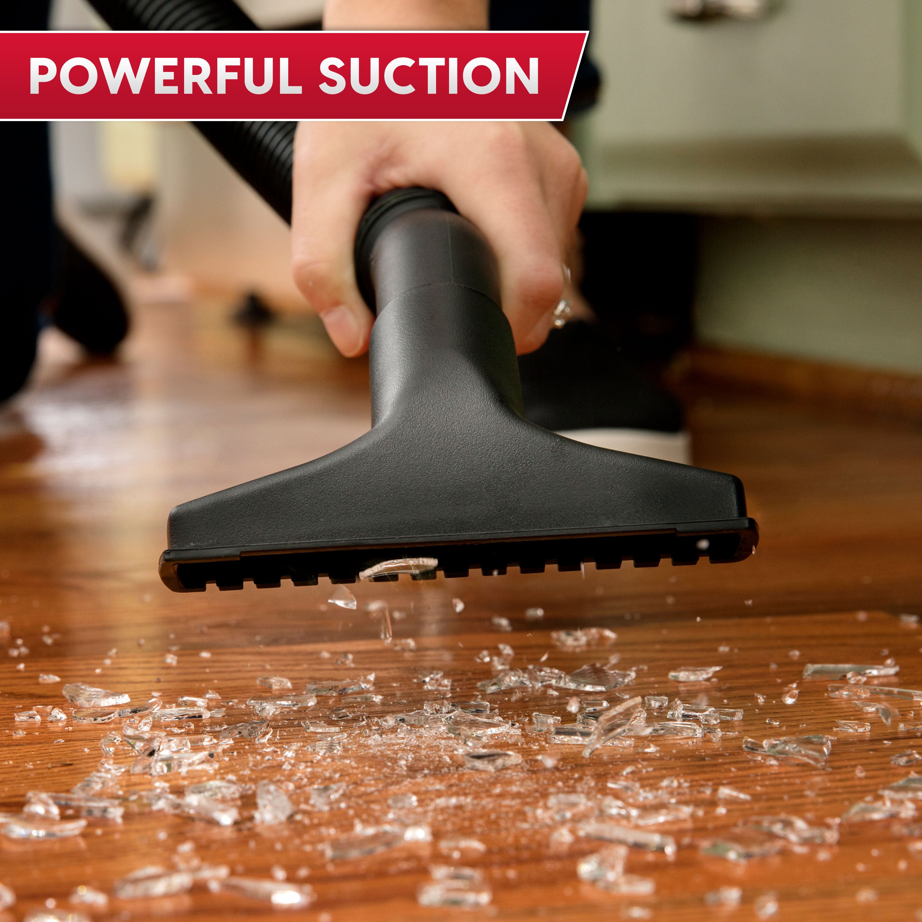Person using a vacuum cleaner on a wooden floor with shattered glass, emphasizing powerful suction.
