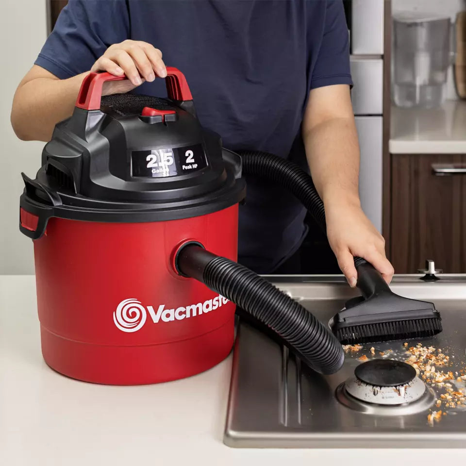 Person using a red and black Vacmaster vacuum cleaner on a stove.