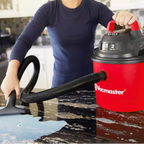 Person using a red Vacmaster vacuum cleaner on a wet floor.