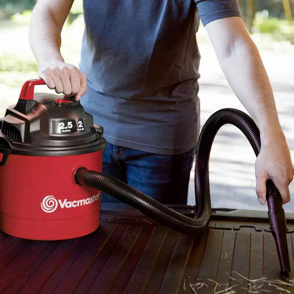 Person using a red Vacmaster vacuum cleaner on a wooden surface.