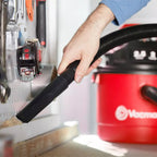 Person using a red vacuum cleaner with a black attachment to clean a kitchen.